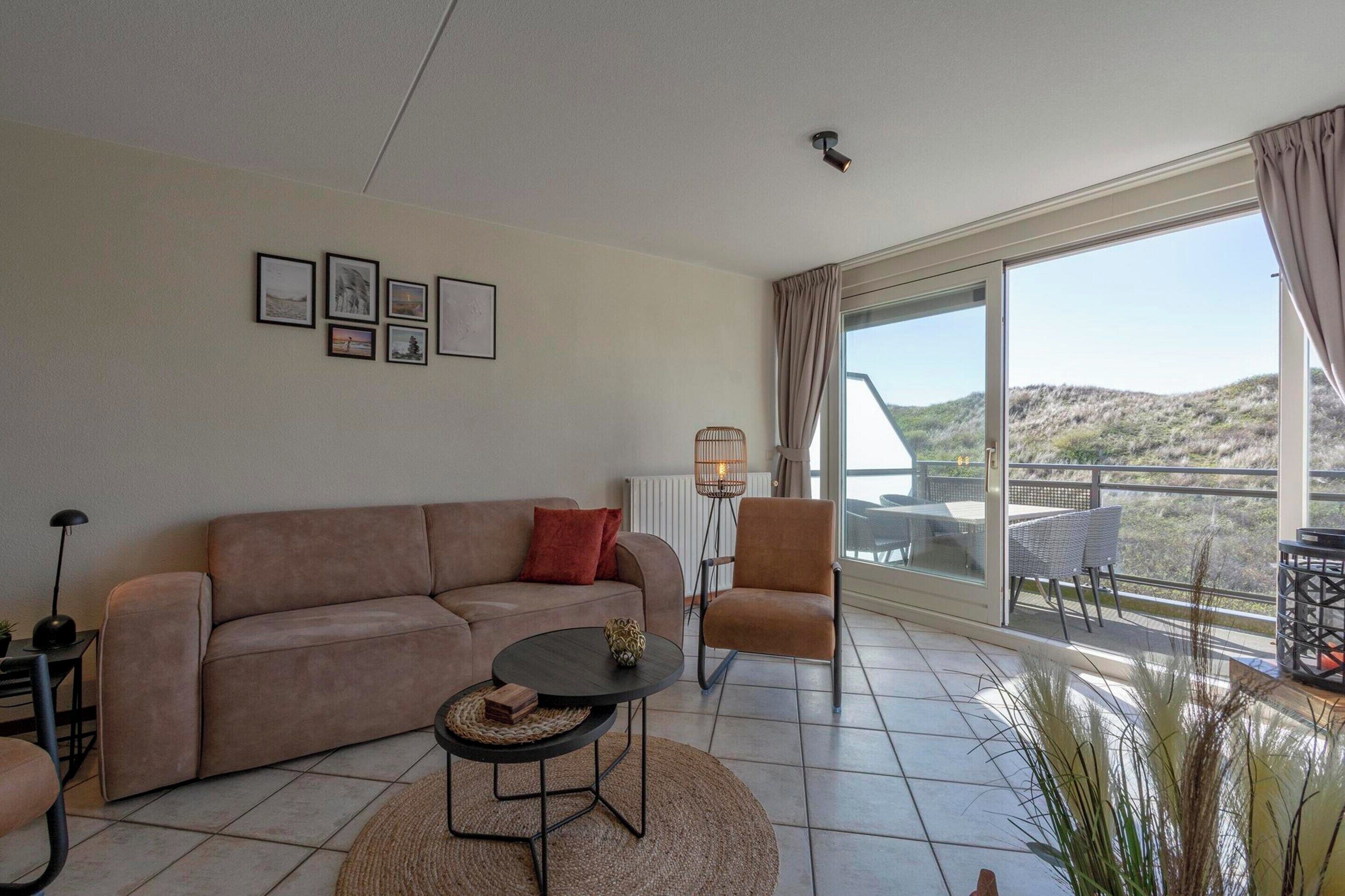 Ein Wohnzimmer mit einer Couch, einem Couchtisch, einem Sessel und einem großen Fenster mit Blick ins Freie.