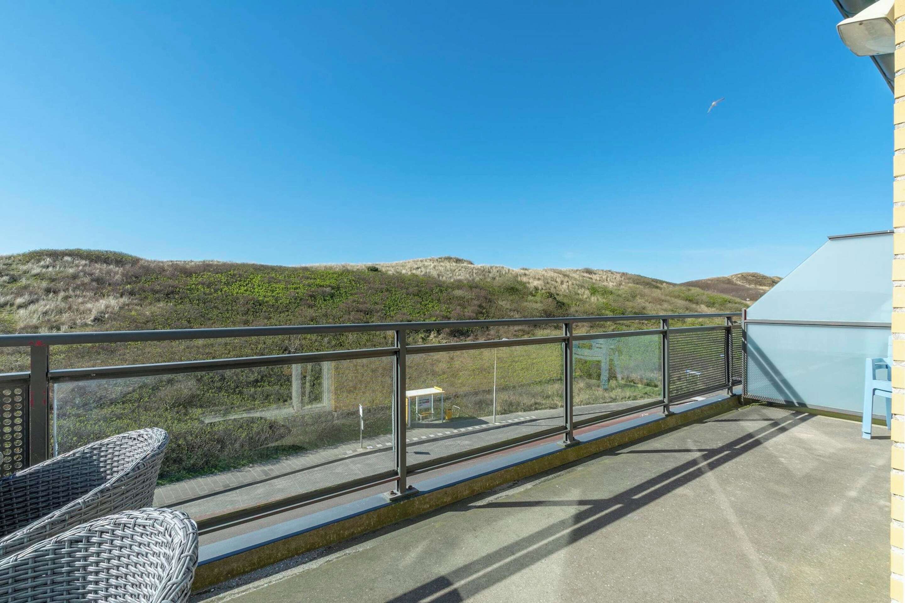 Un balcon avec des fauteuils en osier, une rambarde en métal et une vue sur les collines.