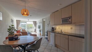 Une cuisine moderne avec des meubles en bois, un four à micro-ondes et un lave-vaisselle. On y trouve également un coin repas avec une table ronde et des chaises.