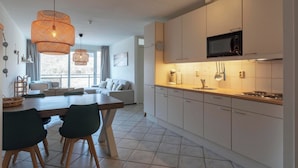 A modern kitchen with white cabinets, a microwave, and a dining area with a wooden table and chairs. - Wijde Blick 212 Apartment in Callanstoog (Callantsoog)