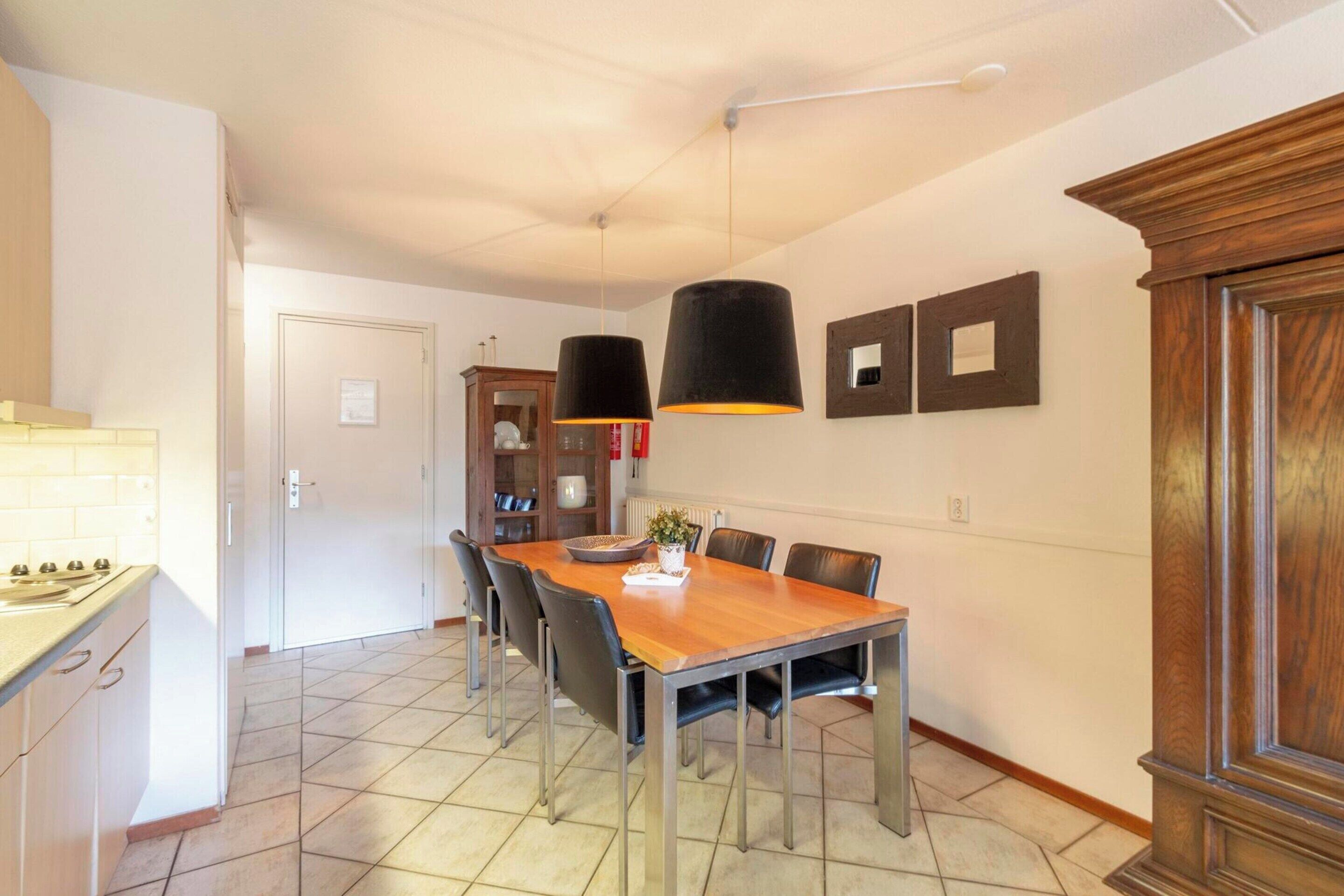 Un espace repas avec une table en bois, des chaises noires et des luminaires suspendus.