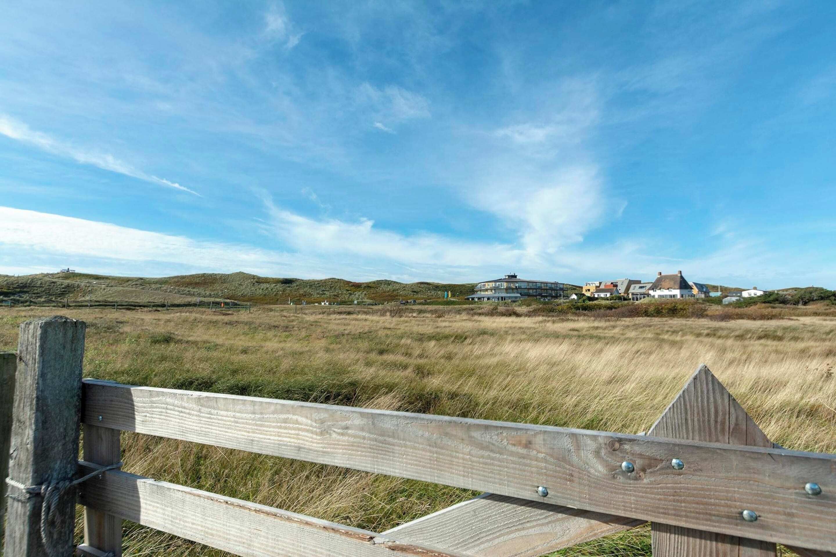 A wooden fence with a view of a coastal landscape, including grassy fields and houses in the distance.