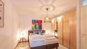 Une chambre à coucher avec un lit, des lampes de chevet, un tableau abstrait aux couleurs vives et des armoires en bois.