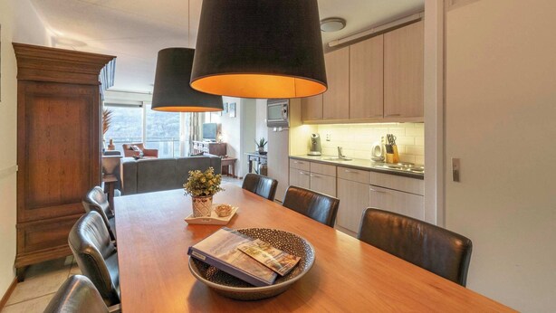 Un espace de salle à manger moderne avec une table en bois, des chaises noires et des luminaires suspendus.