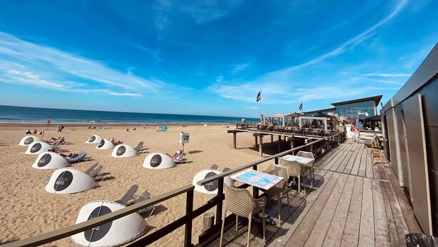 Un ristorante sulla spiaggia con posti a sedere all'aperto e lettini.