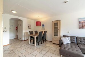 A modern living room with a brown sofa, a dining table with chairs, a red pendant light, and a cabinet with glass doors. - Apartment in Callantsoog by the Beach (Callantsoog)