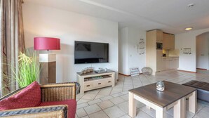 Ein modernes Wohnzimmer mit Flachbildfernseher, Couchtisch aus Holz und einem Korbsessel.