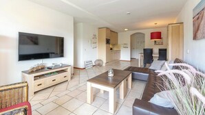 Ein modernes Wohnzimmer mit einem Flachbildfernseher, einem Holztisch, einem braunen Sofa und einem Essbereich mit einer roten Lampe.