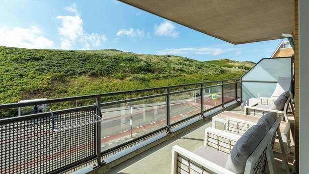Ein Balkon mit Blick auf eine grüne Hügellandschaft, einer Glasuhr und Sitzgelegenheiten mit Kissen.