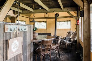 A rustic wooden interior with a round wooden table and wicker chairs, a hanging light fixture, and a fire extinguisher mounted on the wall. - Charming Woodlodge Stay (Callantsoog)