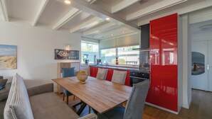 A modern kitchen with a wooden table, red cabinets, and a view of the city. - Modern Home Near Beach (Sint Maartensvlotbrug)