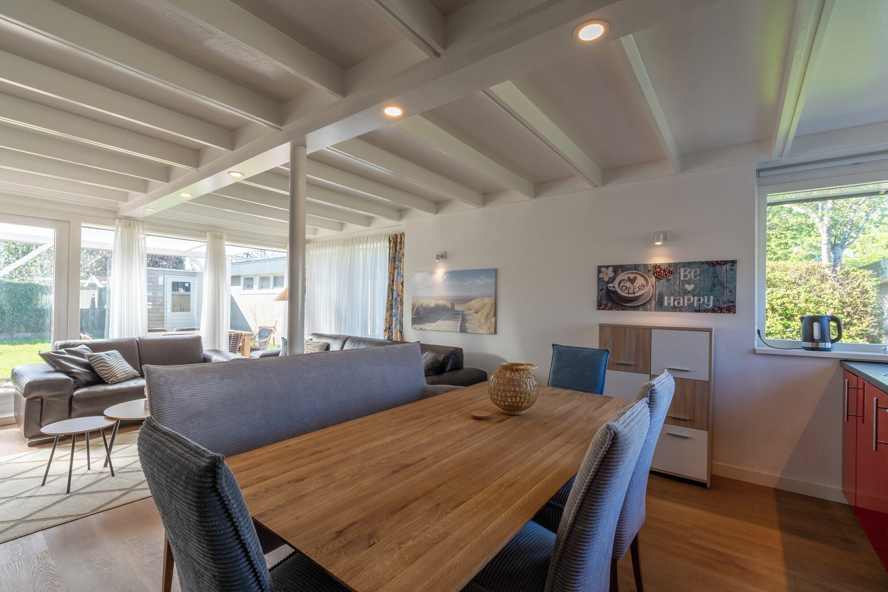 A spacious living area with a wooden dining table, grey upholstered chairs, a grey sofa, and a small side table.