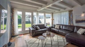 A modern living room with a sectional sofa, a coffee table, and a large window with curtains. - Modern Home Near Beach (Sint Maartensvlotbrug)