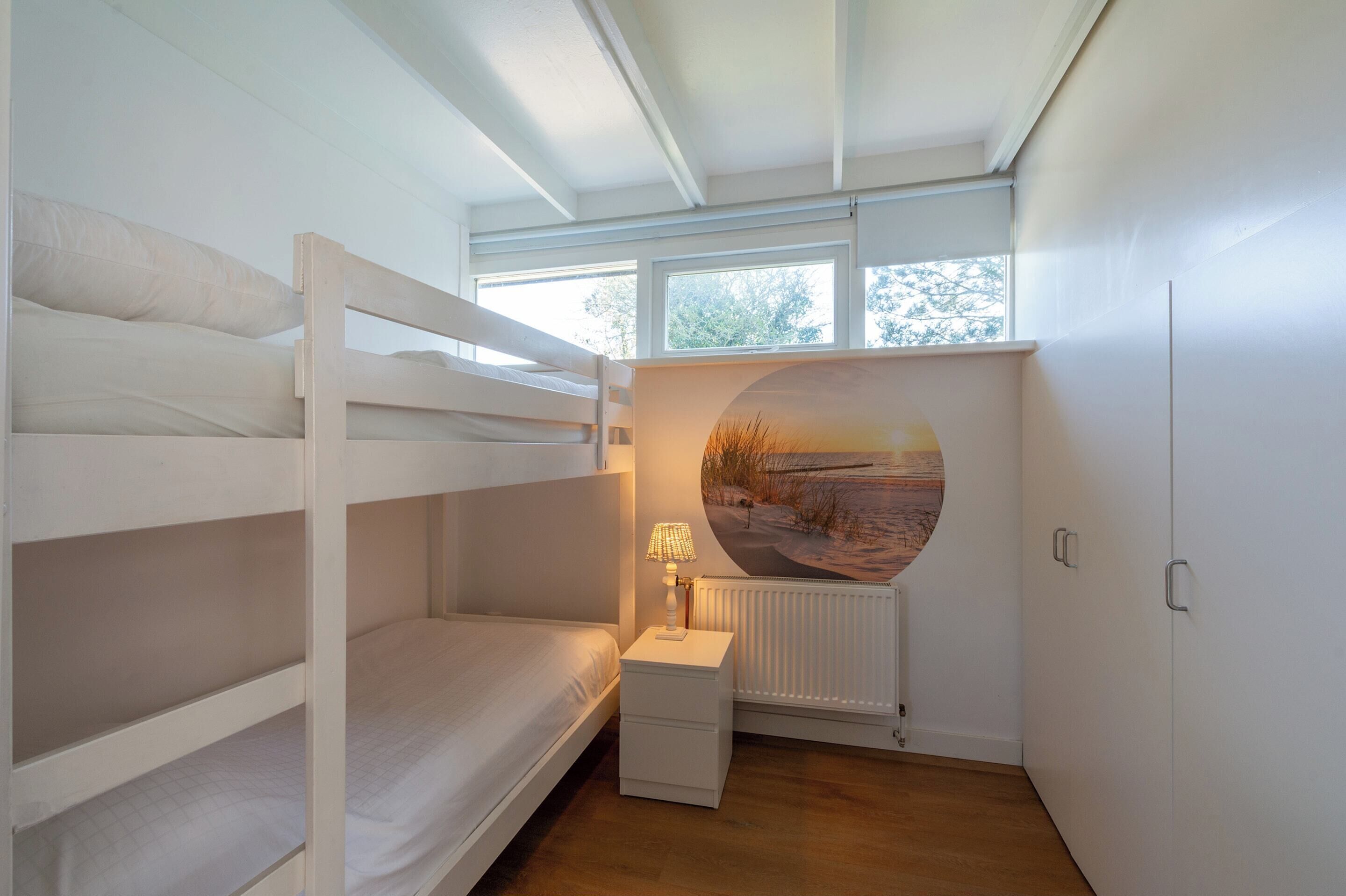 Ein Schlafraum mit Etagenbett, Nachttisch, Lampe, Heizkörper und einem großen, runden Fenster mit schöner Aussicht.