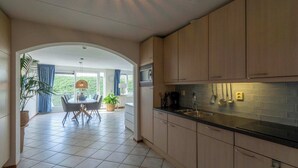 Une cuisine moderne avec des meubles de couleur bois clair, un plan de travail noir et un coin repas comprenant une table et des chaises.