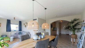 Un espace repas moderne avec une table en bois, des chaises grises et deux lampes en osier suspendues.
