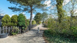 A gravel pathway flanked by wooden fences and dense greenery, leading to a building with a visible entrance. - Wildrijk 83 Holiday Home Near Beach (Sint Maartensvlotbrug)
