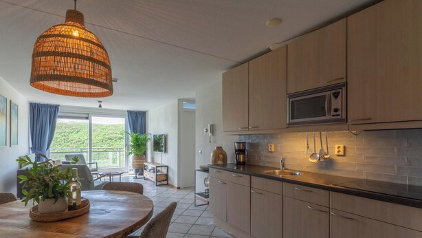 A modern kitchen with wooden cabinets, a microwave, and a hanging light fixture. - Wijde Blick 310 Apartment Near Callanstoog Beach (Callantsoog)