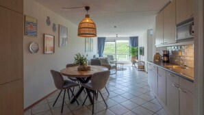 A modern kitchen with a dining area, featuring a round table, chairs, and a hanging light fixture. - Wijde Blick 310 Apartment Near Callanstoog Beach (Callantsoog)
