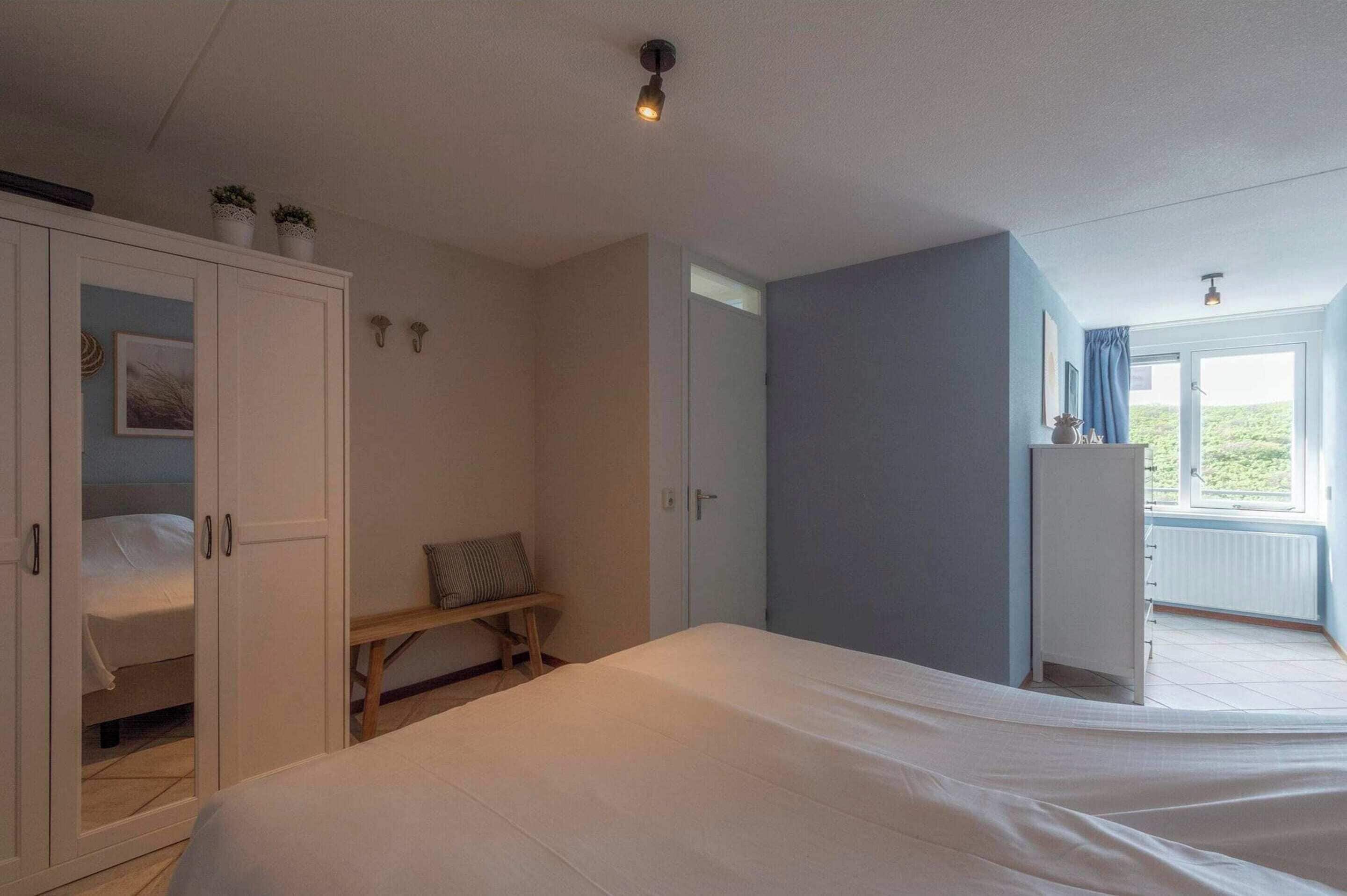 A bedroom with a bed, a wardrobe, a bench, and a window with a view.