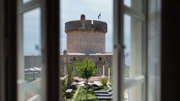 A view of a castle-like structure with a flag on top, a swimming pool, and lounge chairs in the foreground.