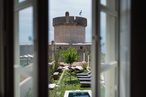 A view of a castle-like structure with a flag on top, a swimming pool, and lounge chairs in the foreground. - Spindler Luxury rooms by DuHomes (Dubrovnik)