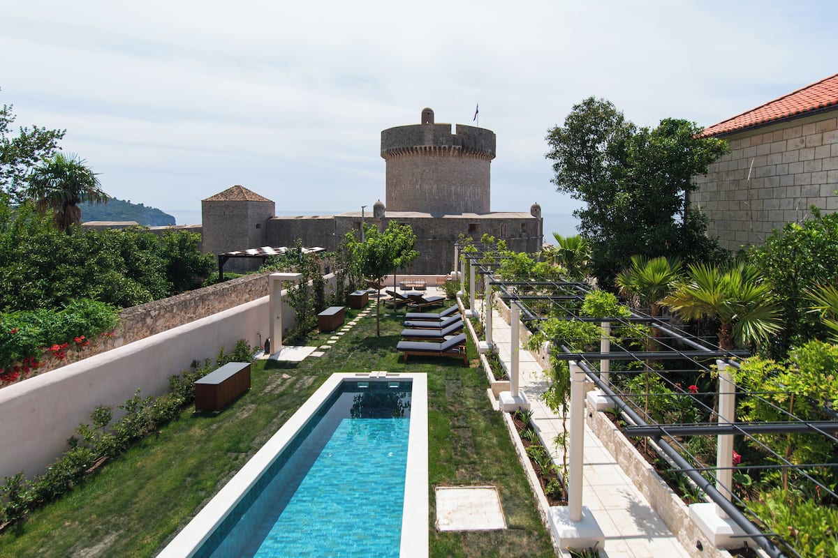 Una piscina, sillas de descanso y una estructura que parece un castillo al fondo.