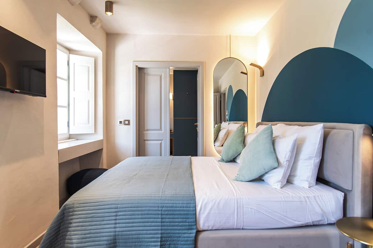 Una habitación de hotel moderna con una cama grande, una mesita de noche, un espejo y una ventana.