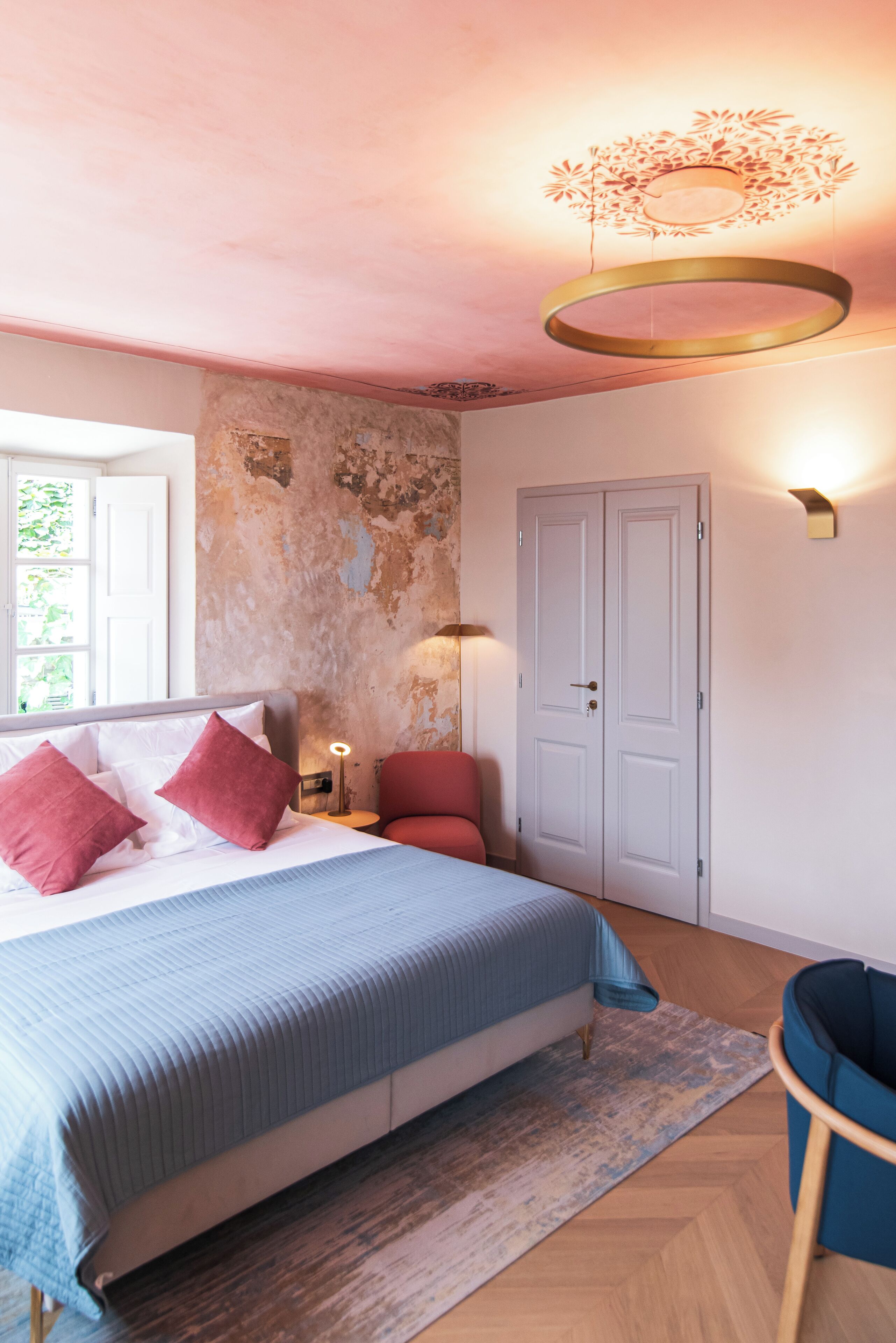 A bedroom with a large bed, a red chair, a wooden floor, and a white door.