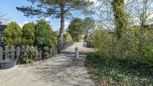Un sentier bordé d’arbres et délimité par une clôture en bois, qui mène à un bâtiment.