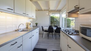 Une cuisine moderne avec des meubles blancs, un évier en acier inoxydable, une cuisinière à gaz et un coin repas comprenant une table et des chaises.