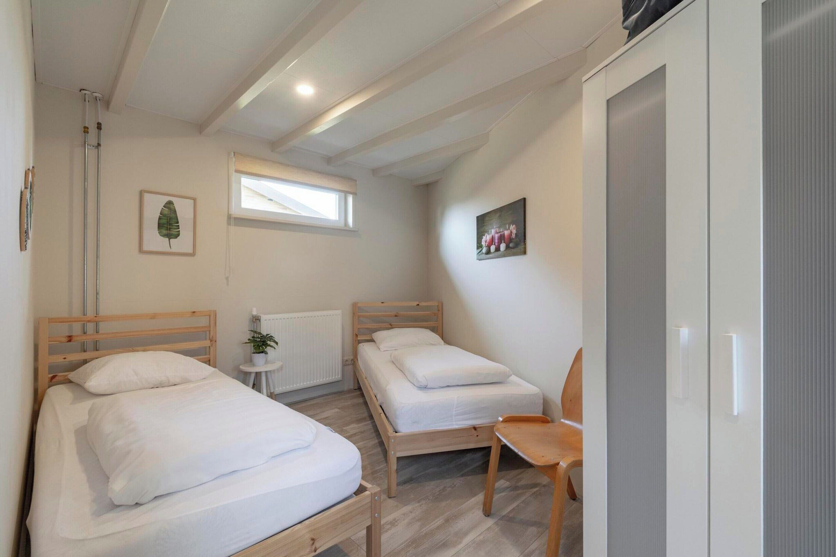 A small, well-lit bedroom with two single beds, a wooden chair, a small table, and a radiator.