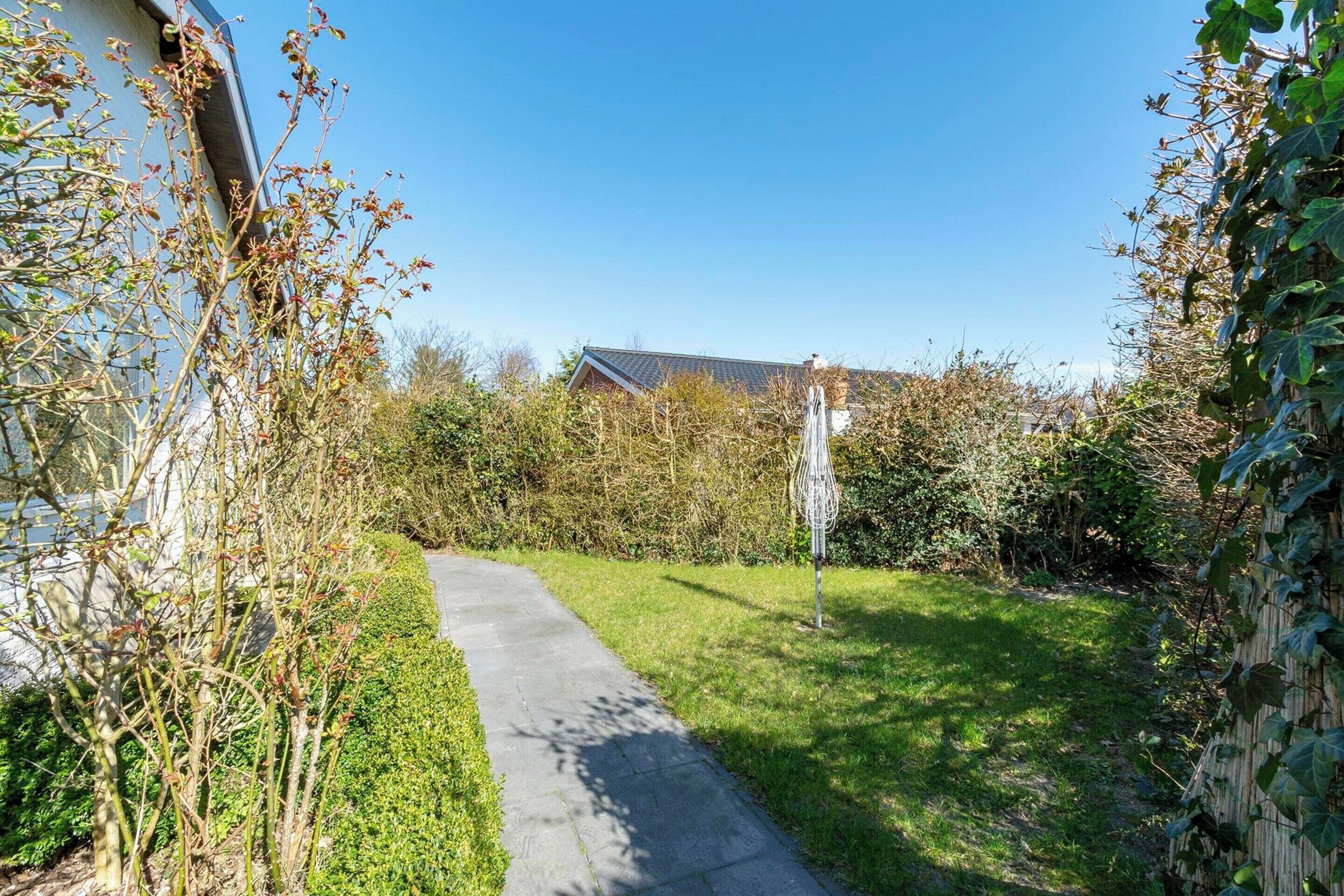 A paved pathway leading through a garden with a house in the background.