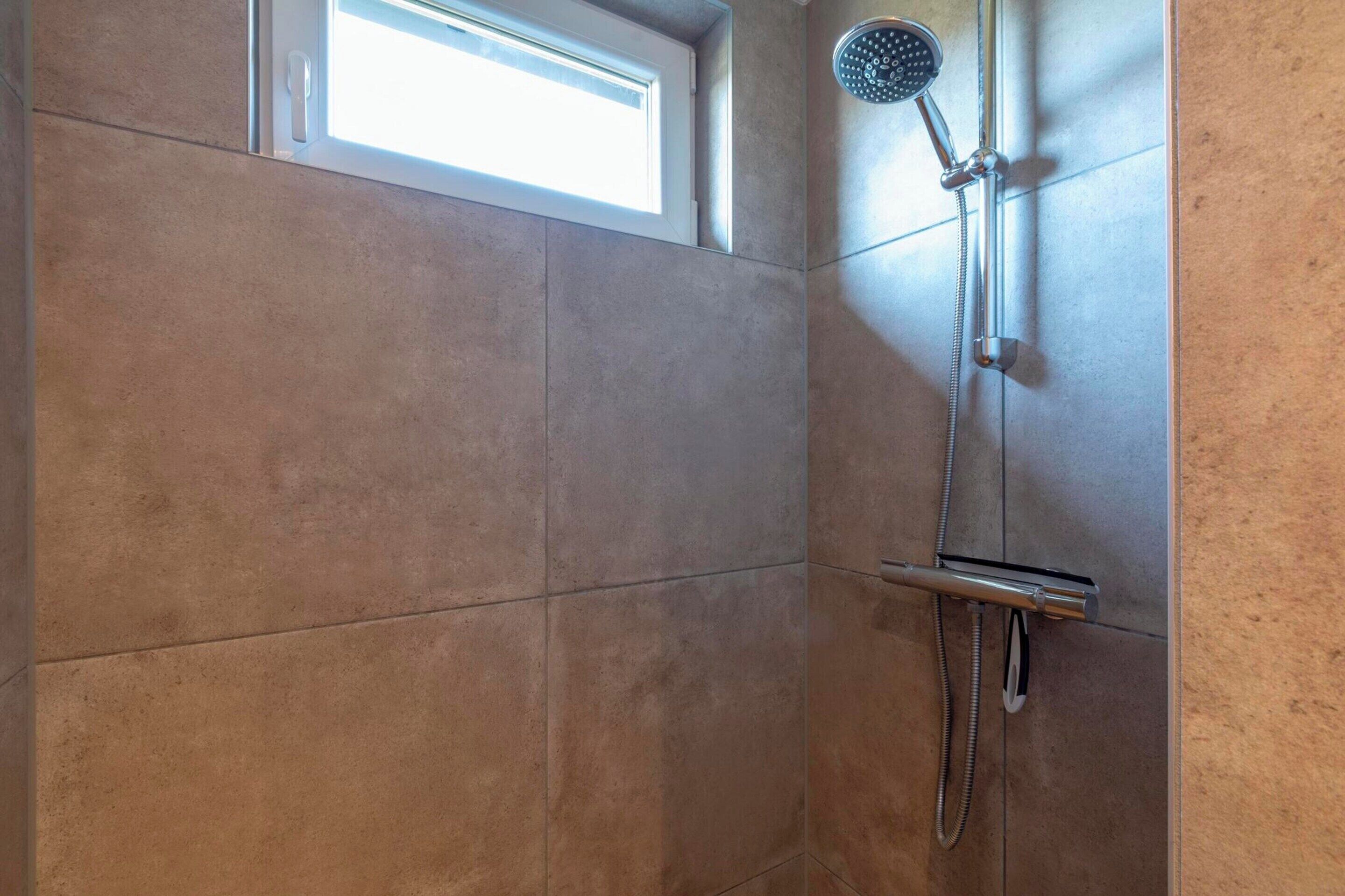 A shower with a handheld showerhead and a wall-mounted faucet, tiled walls, and a window above the shower.