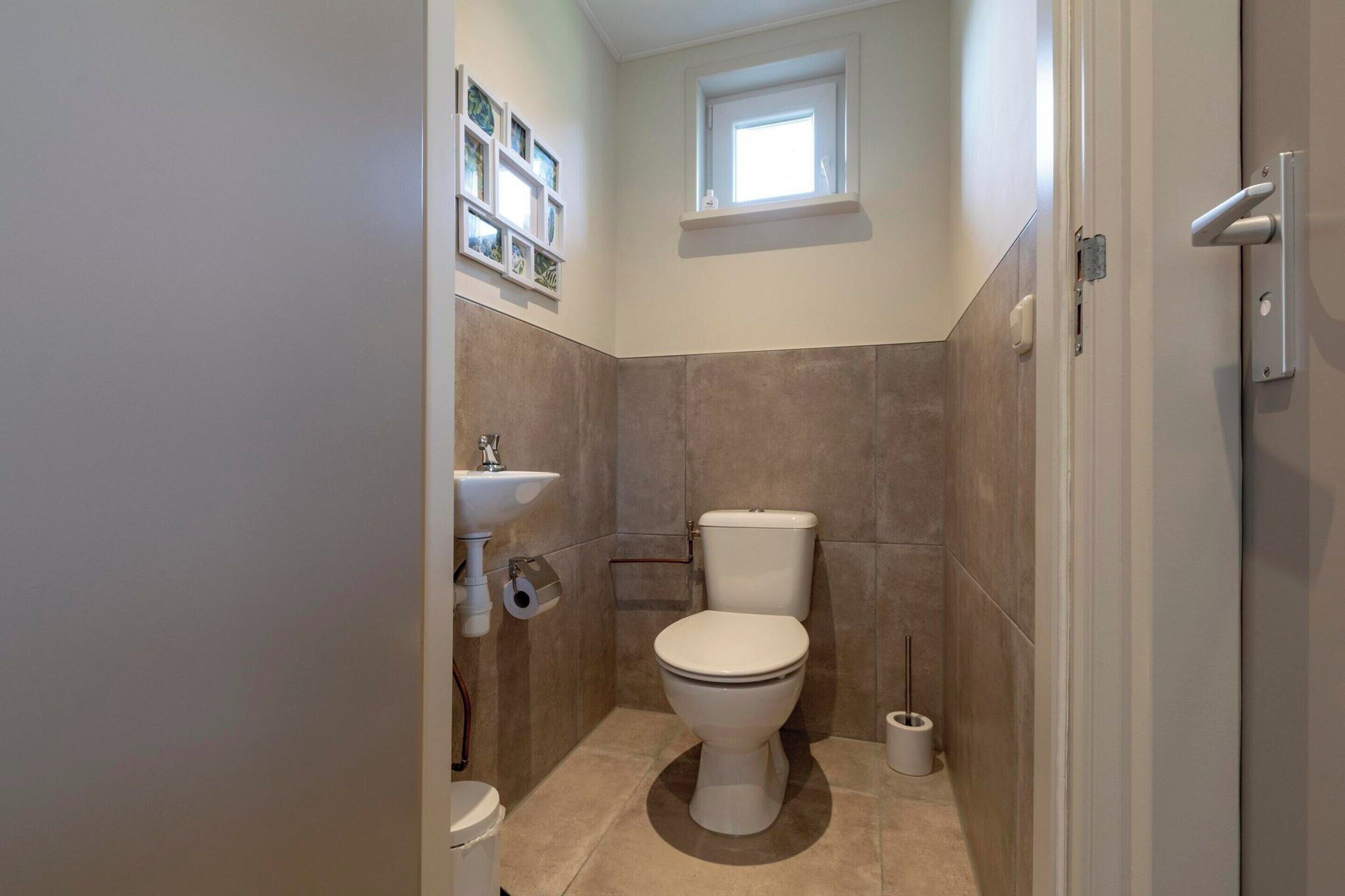 A small bathroom with a toilet, sink, and a window above the toilet.