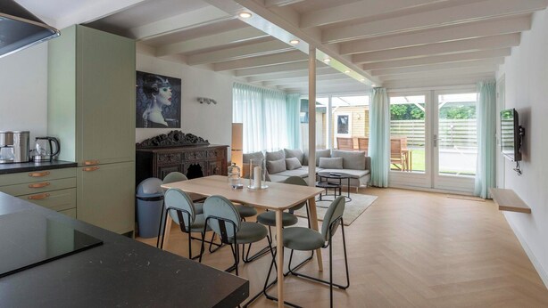 A modern kitchen with a dining area, a sofa set, and a TV mounted on the wall. - Bungalow Near Sint Maartenszee Beach (Sint Maartensvlotbrug)