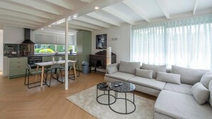 A modern living room with a sofa, two round tables, a dining area with chairs, and a kitchen in the background. - Bungalow Near Sint Maartenszee Beach (Sint Maartensvlotbrug)