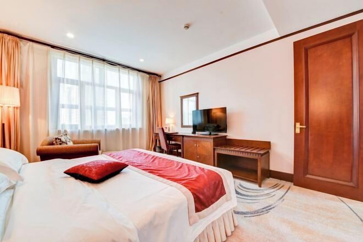 A hotel room with a bed, a desk, a television, and a door.