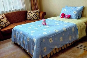 A bedroom with a bed covered in a blue floral bedspread, a brown sofa with patterned cushions, and a small pink Hello Kitty toy on the bed. - Longtang Hotel (Harbin)