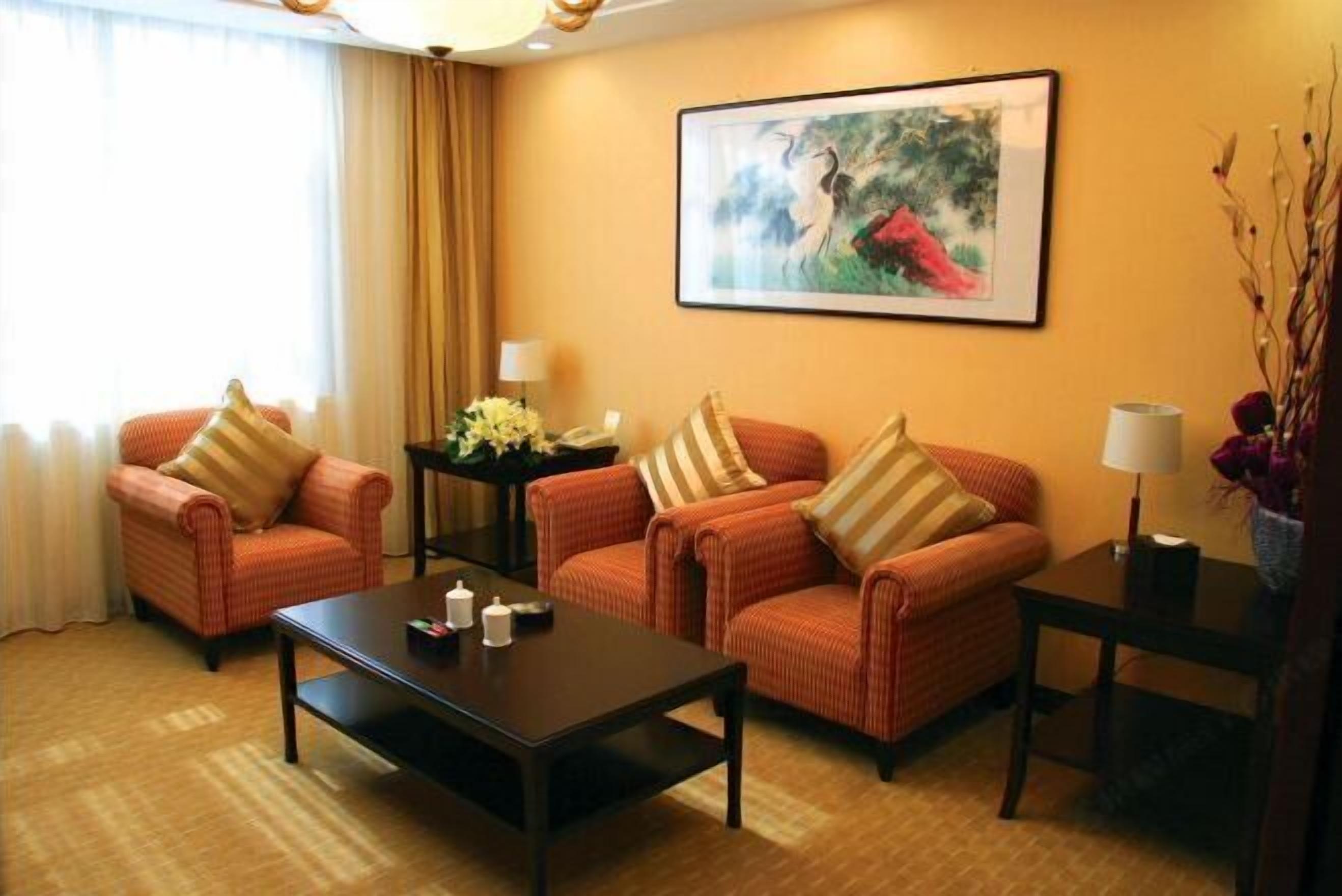 Habitación de hotel con dos sofás, una mesa de centro, una mesita auxiliar, una lámpara, un cuadro en la pared y una ventana con cortinas.