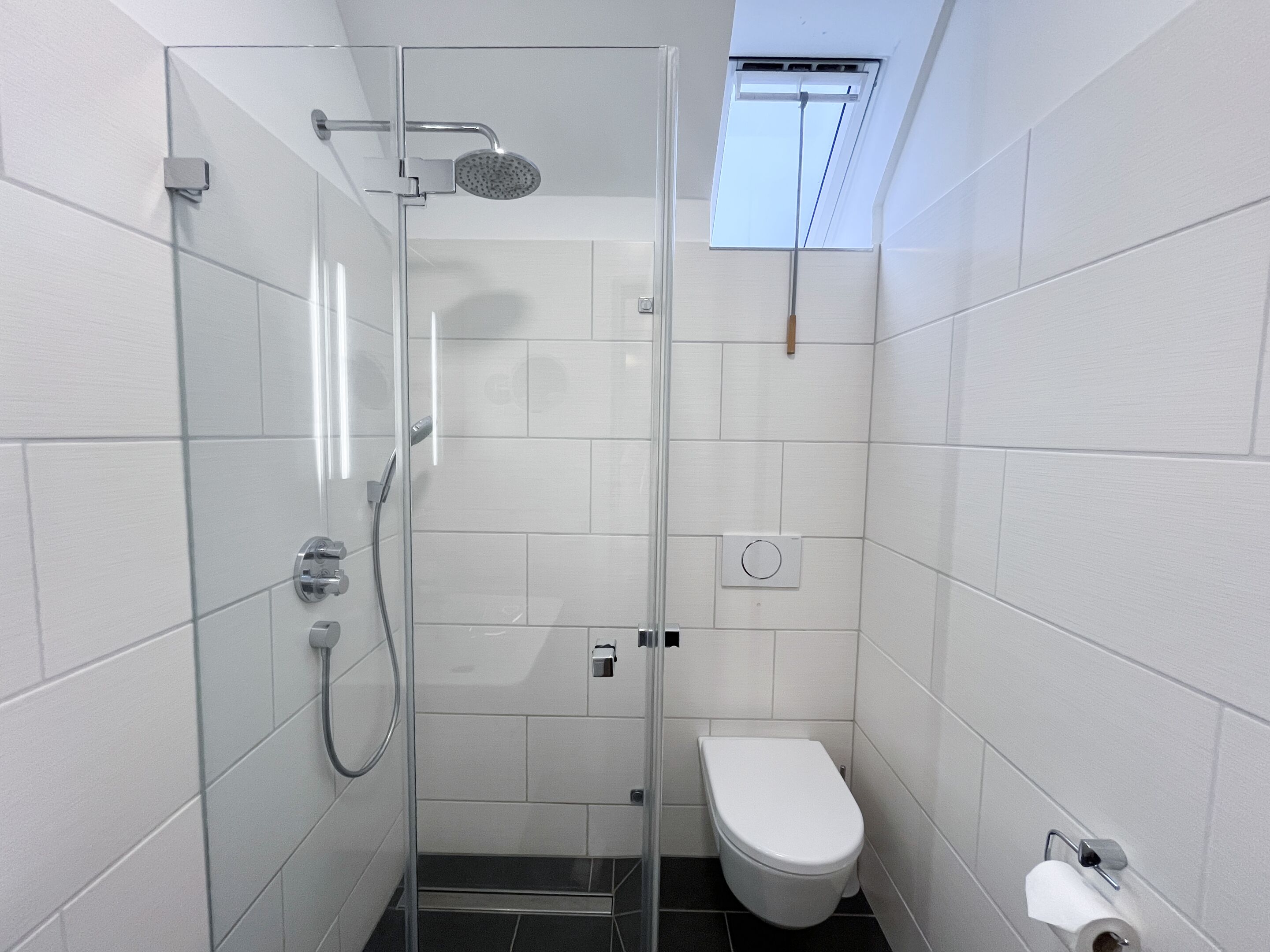 Un baño pequeño y moderno con cabina de ducha de vidrio, inodoro y ventana.