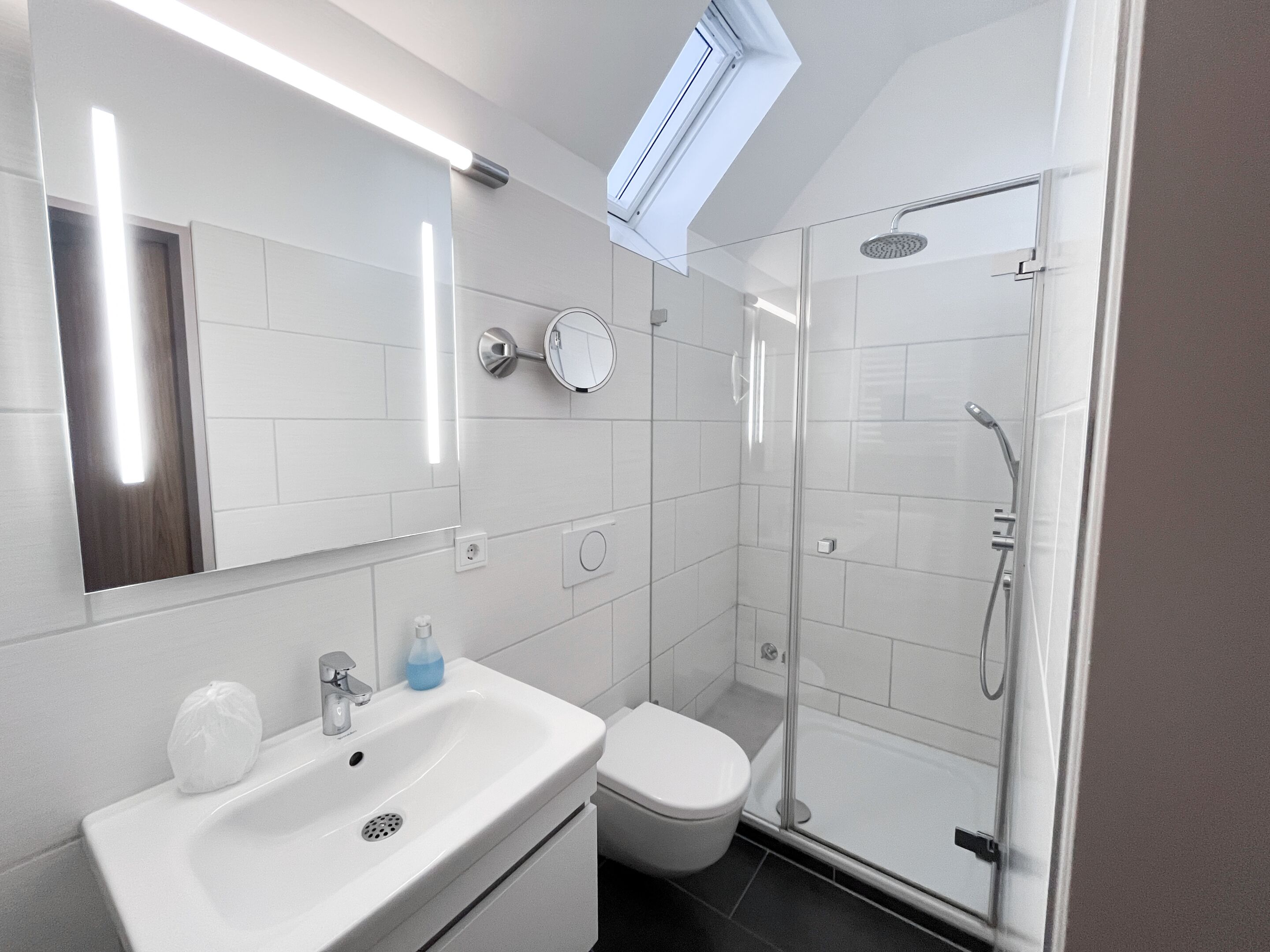 Ein modernes Badezimmer mit einer Duschkabine, einem weißen Waschbecken und einer Toilette.