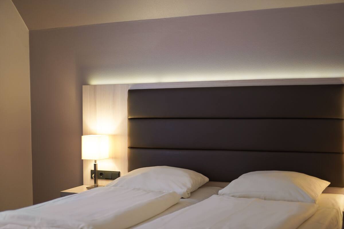 A hotel room with a bed, a nightstand, and a lamp.