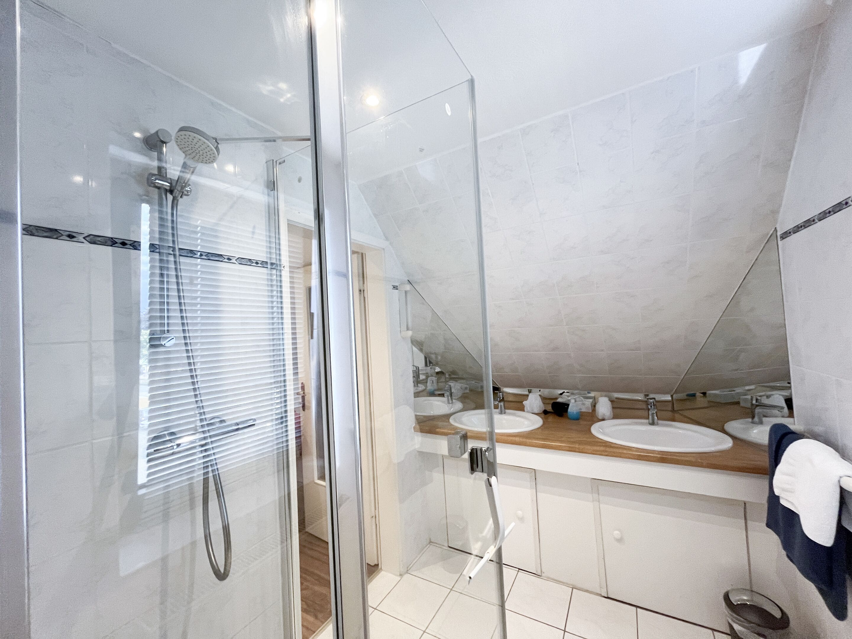 A modern bathroom with a glass-enclosed shower, two sinks, and a towel rack.