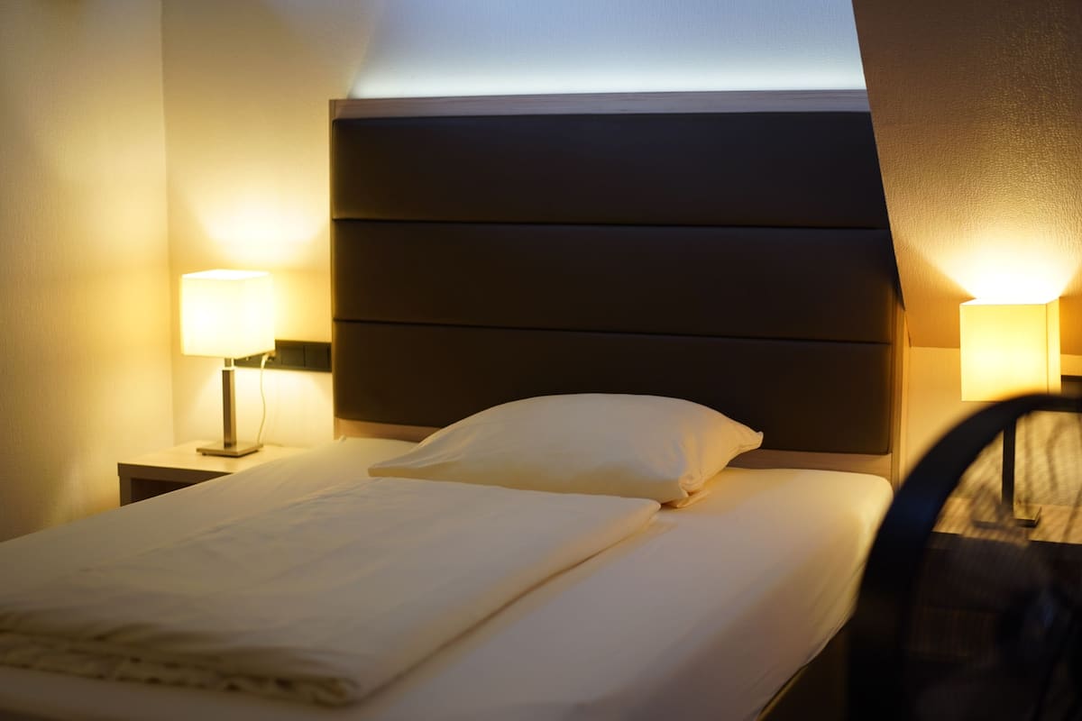 A neatly made bed with a headboard, two bedside lamps, and a chair partially visible.