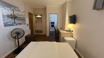 Habitación de hotel con cama, escritorio con lámpara, televisión, ventilador y armario.