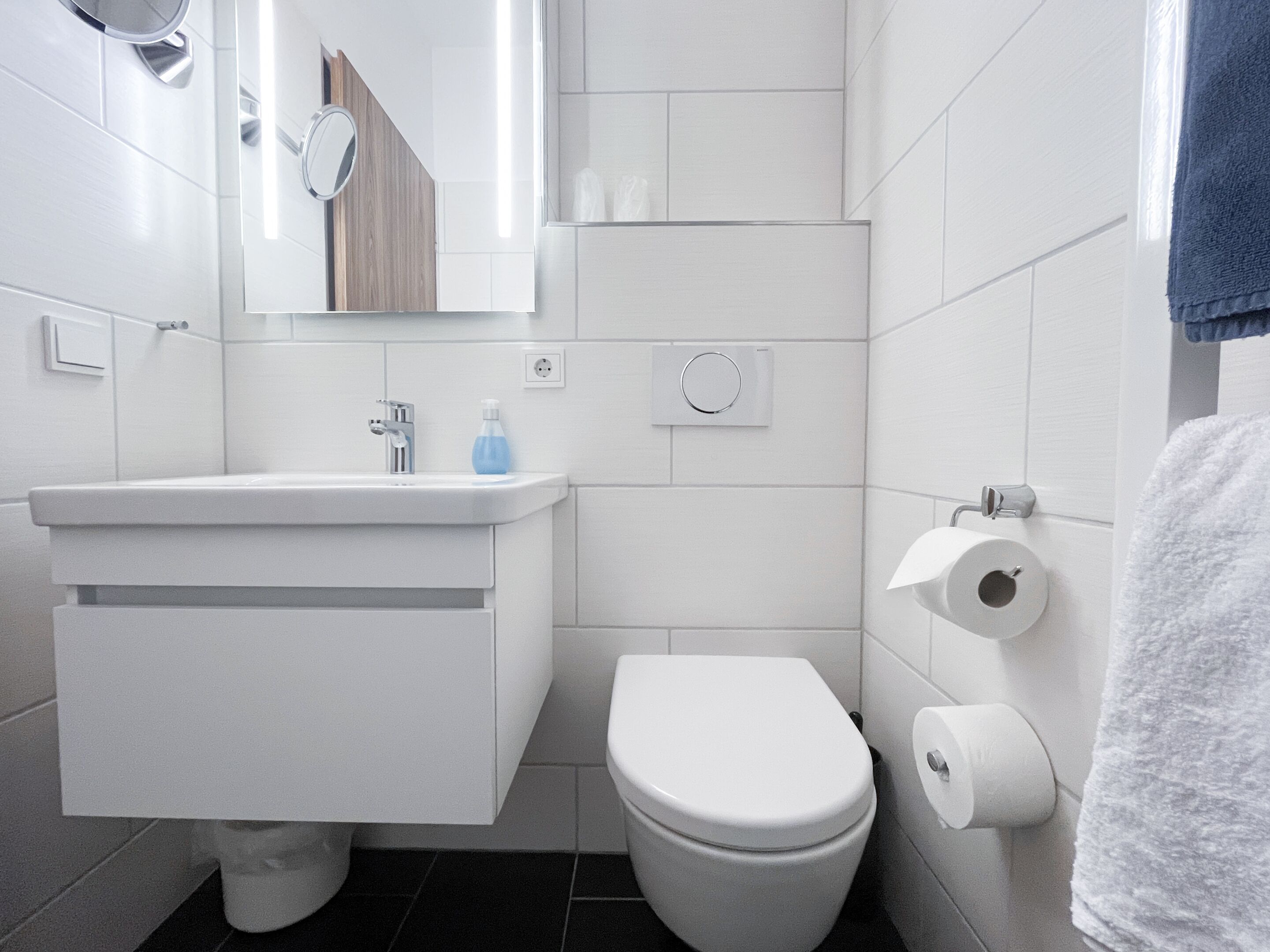 A modern bathroom with a white sink, mirror, and toilet.