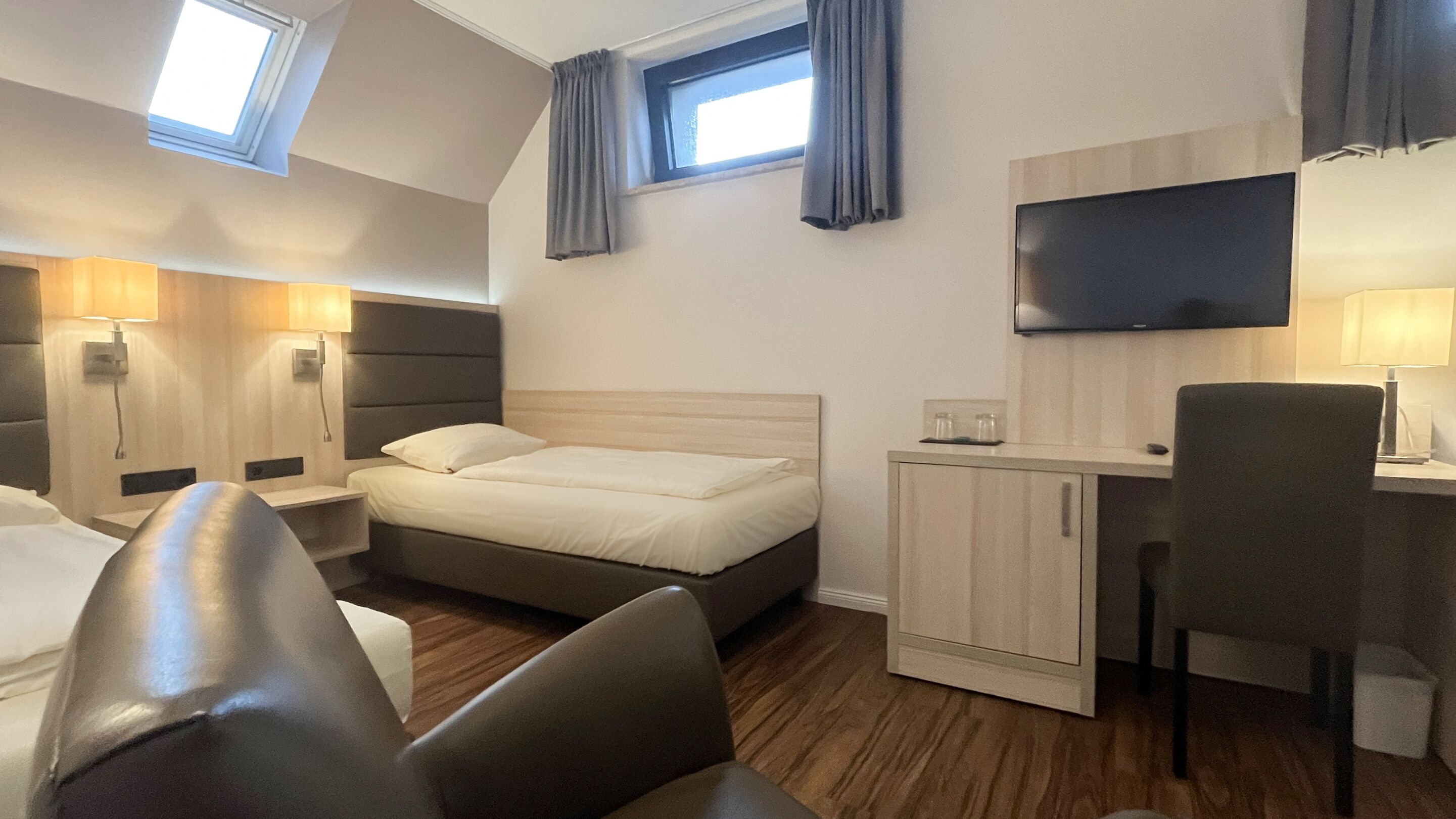 Een hotelkamer met een bed, een bureau, een stoel, een televisie en een raam met gordijnen.