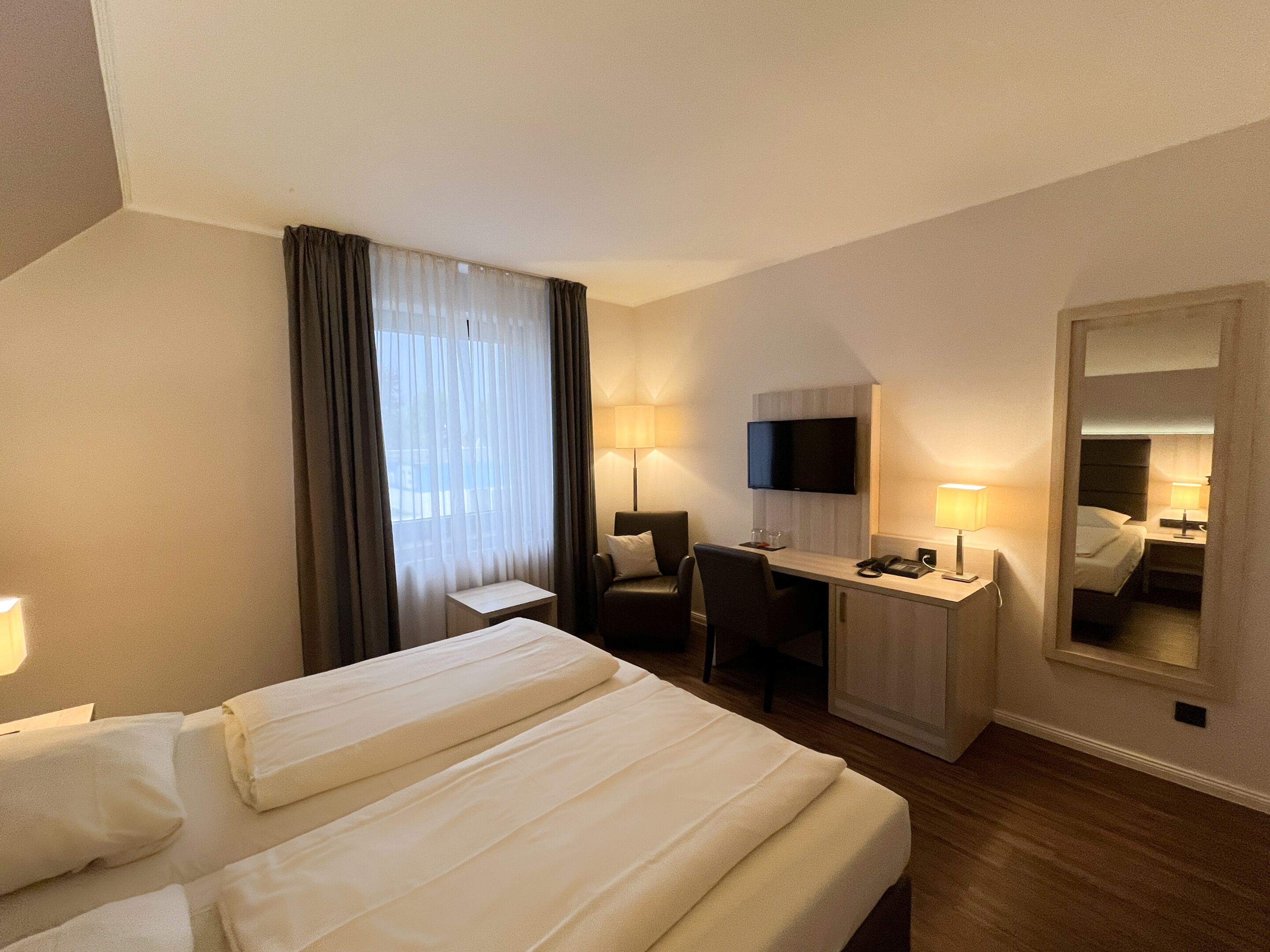 Une chambre d’hôtel avec deux lits, un bureau, une chaise, une télévision et un miroir.