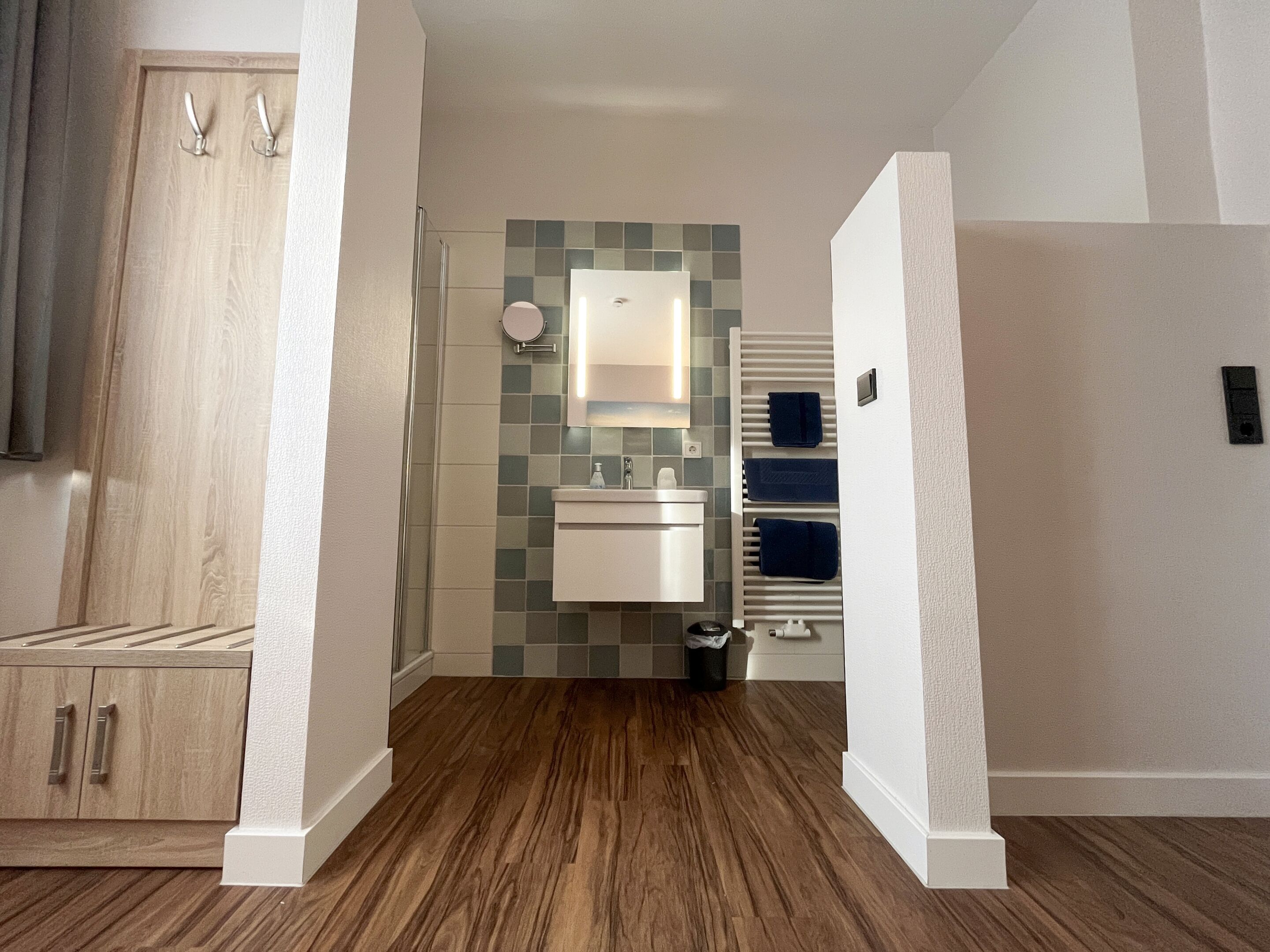 A modern bathroom with a wooden floor, a white sink, a mirror, and a towel rack.